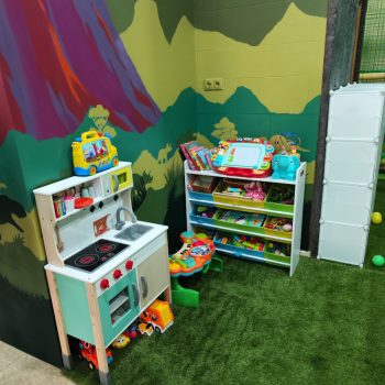 Zona de juegos infantil con cocinita y estanterías de juguetes y libros para cumpleaños infantiles